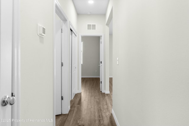 hallway featuring wood finished floors, visible vents, and baseboards