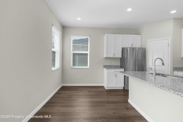 kitchen with light stone counters, dark wood-style floors, white cabinets, a sink, and baseboards