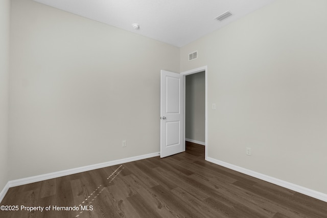 empty room with dark wood-style floors, visible vents, and baseboards