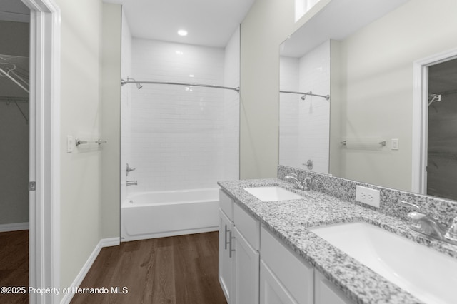 full bathroom with a walk in closet, double vanity, a sink, and wood finished floors