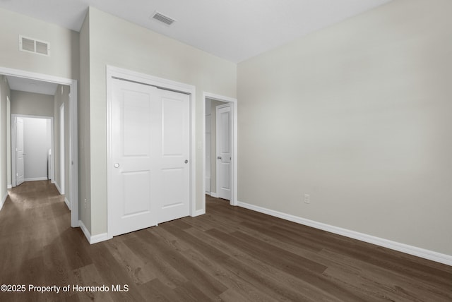 unfurnished bedroom with dark wood-type flooring, a closet, visible vents, and baseboards