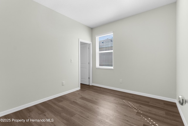 spare room featuring dark wood-type flooring and baseboards