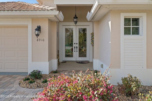 property entrance featuring a garage, french doors, and stucco siding