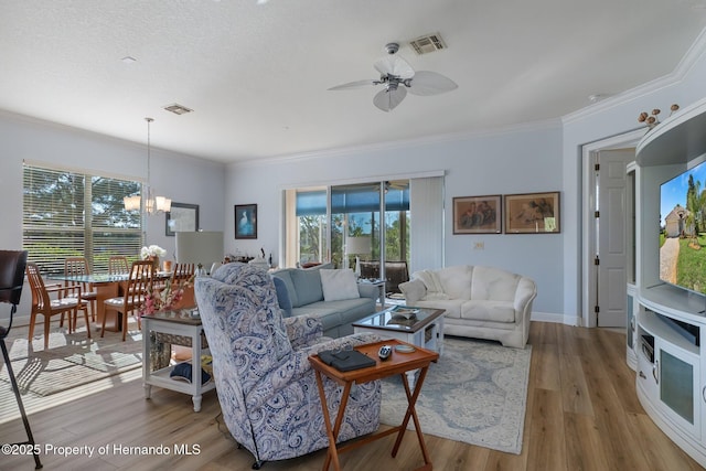 living area featuring baseboards, visible vents, wood finished floors, crown molding, and ceiling fan with notable chandelier