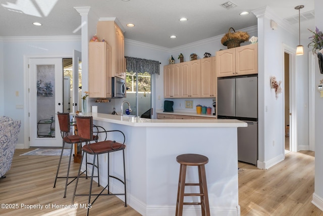 kitchen with appliances with stainless steel finishes, a breakfast bar, a peninsula, and light brown cabinetry