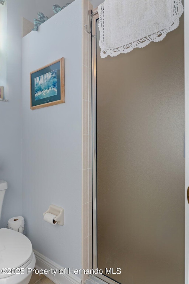 bathroom featuring toilet, a stall shower, and baseboards