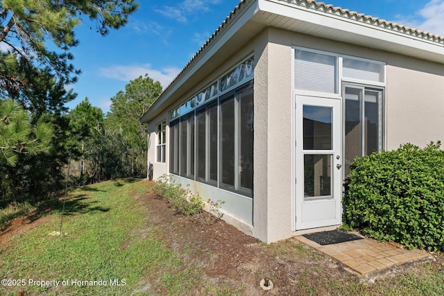 view of side of home with a sunroom, a yard, and stucco siding