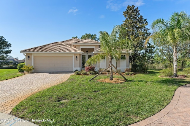 mediterranean / spanish-style house with a garage, a tiled roof, decorative driveway, stucco siding, and a front lawn