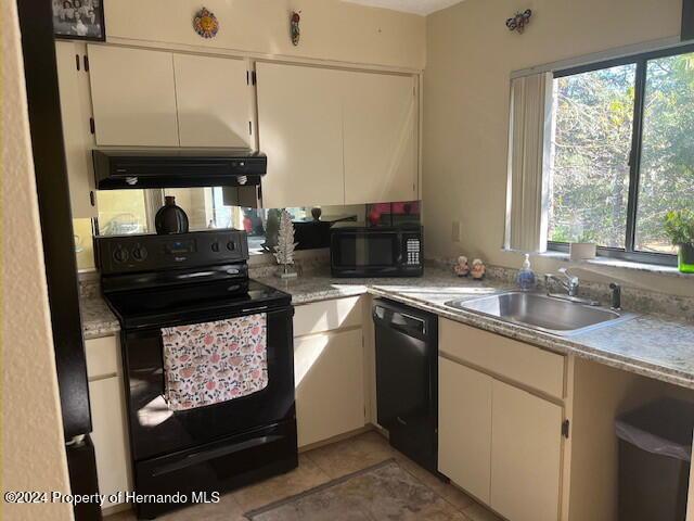 kitchen with light countertops, a sink, under cabinet range hood, and black appliances