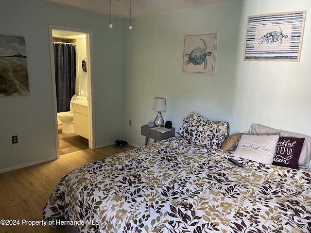 bedroom with connected bathroom, baseboards, and wood finished floors