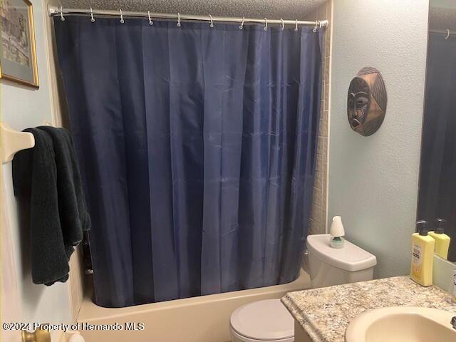 bathroom with a textured wall, shower / bathtub combination with curtain, toilet, a textured ceiling, and vanity