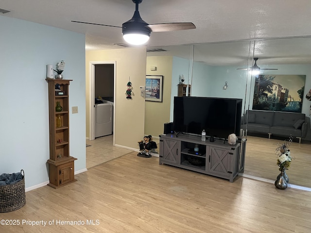 living room featuring washer / clothes dryer, ceiling fan, and light wood-style flooring