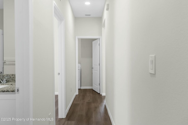 hallway with dark wood-style flooring, a sink, visible vents, baseboards, and washer / clothes dryer