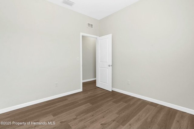 empty room featuring dark wood-style floors, visible vents, and baseboards