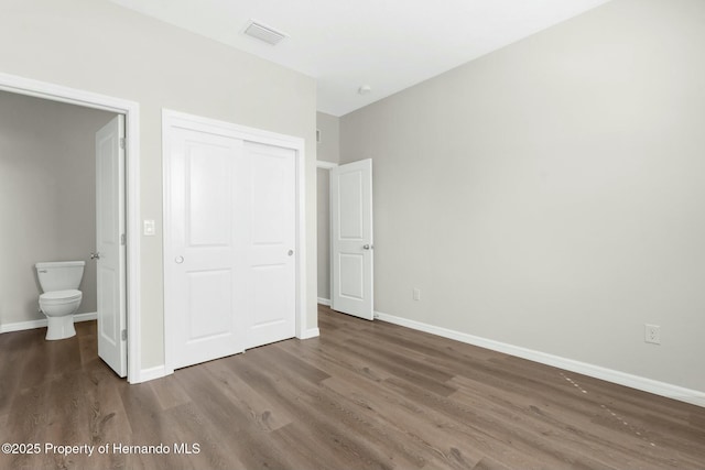 unfurnished bedroom with baseboards, visible vents, connected bathroom, dark wood finished floors, and a closet