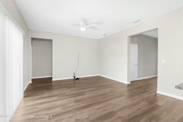 empty room featuring ceiling fan, visible vents, baseboards, and wood finished floors