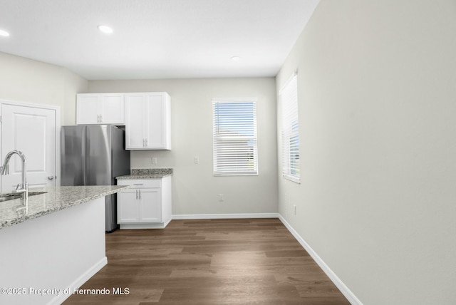 kitchen with light stone counters, dark wood-type flooring, white cabinetry, a sink, and baseboards