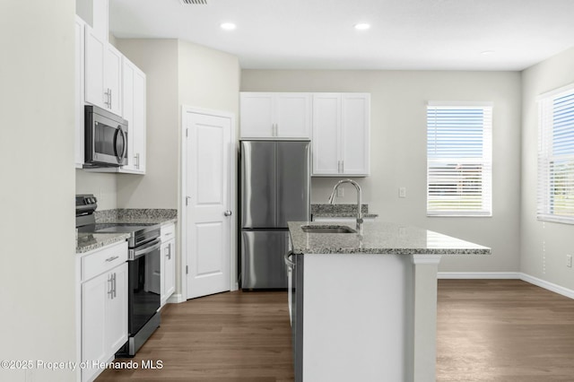 kitchen with light stone countertops, a kitchen island with sink, stainless steel appliances, white cabinetry, and a sink