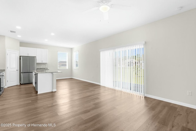 interior space with visible vents, white cabinetry, open floor plan, stainless steel refrigerator, and a center island with sink