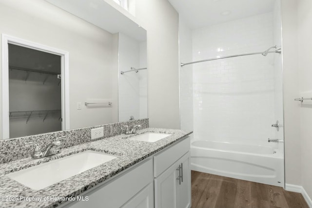 full bath featuring a walk in closet, bathtub / shower combination, a sink, and wood finished floors