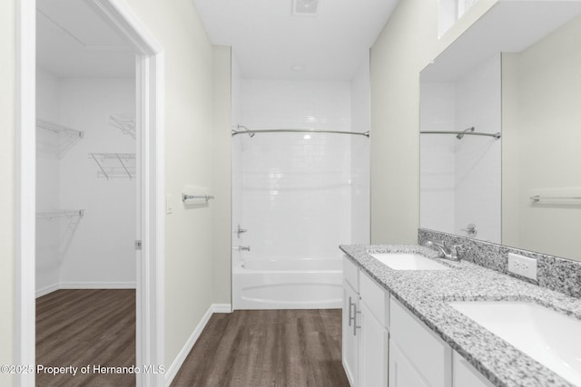 bathroom featuring double vanity, wood finished floors, a spacious closet, and a sink