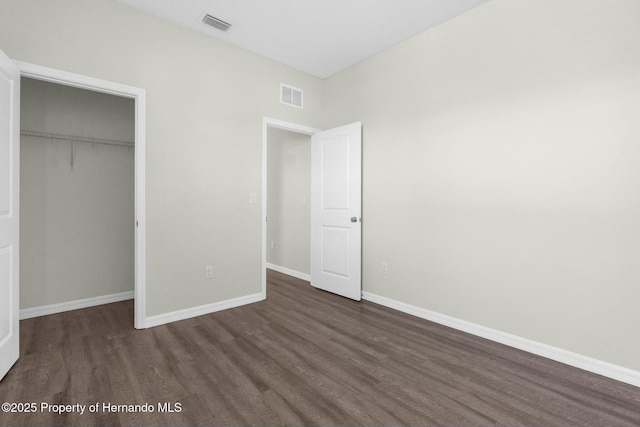 unfurnished bedroom featuring a closet, dark wood finished floors, visible vents, and baseboards