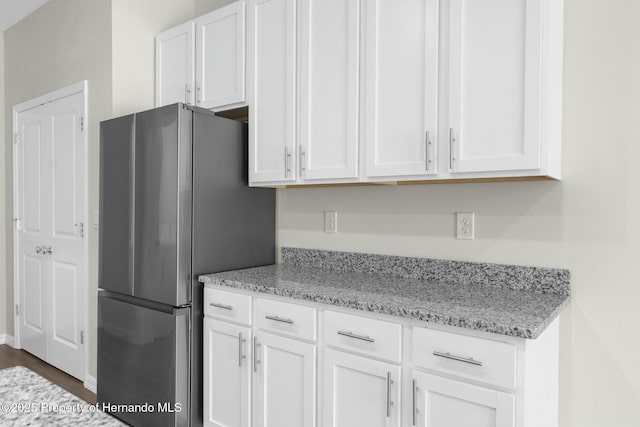 kitchen featuring light stone countertops, freestanding refrigerator, and white cabinets