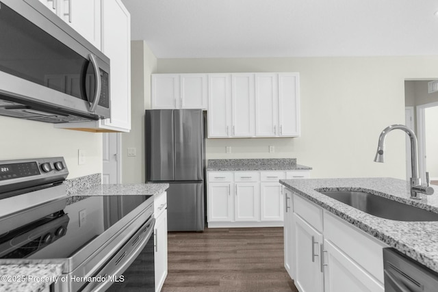 kitchen with appliances with stainless steel finishes, a sink, light stone countertops, and white cabinets