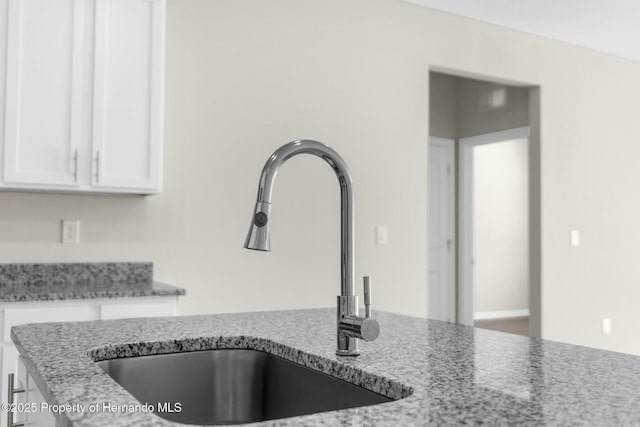 room details with white cabinets, a sink, and light stone countertops