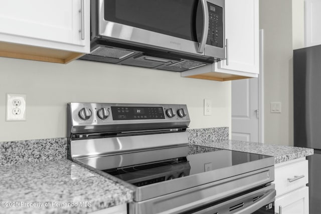 kitchen with stainless steel appliances, white cabinets, and light stone countertops