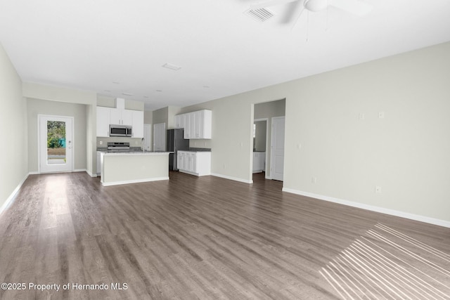 unfurnished living room with a ceiling fan, dark wood-style flooring, visible vents, and baseboards