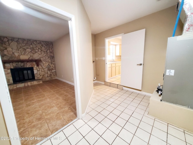 interior space featuring light tile patterned floors, baseboards, and a stone fireplace