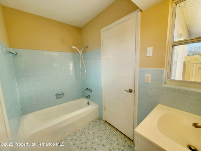 full bath with tile walls, washtub / shower combination, wainscoting, a sink, and tile patterned flooring