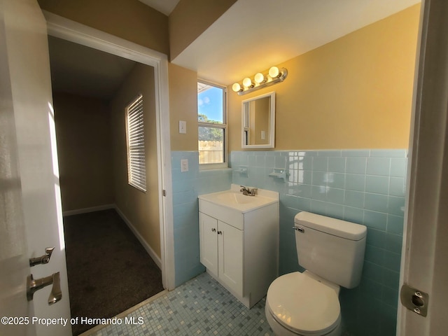 bathroom with tile patterned flooring, toilet, vanity, tile walls, and wainscoting