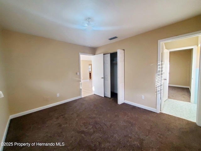 unfurnished bedroom with dark colored carpet, a closet, visible vents, and baseboards