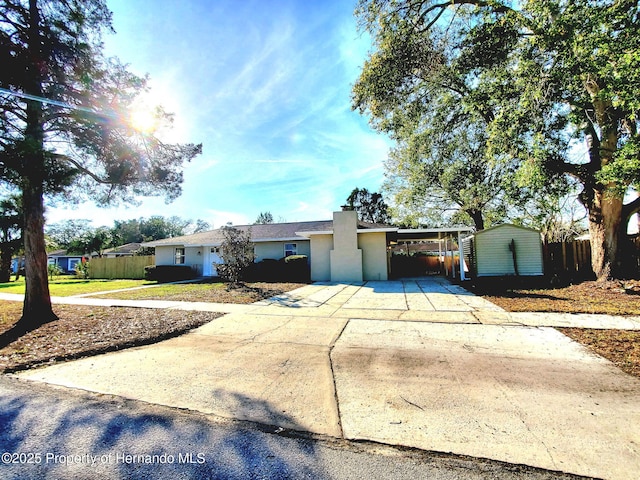 ranch-style house featuring driveway, an attached carport, an outdoor structure, a shed, and stucco siding