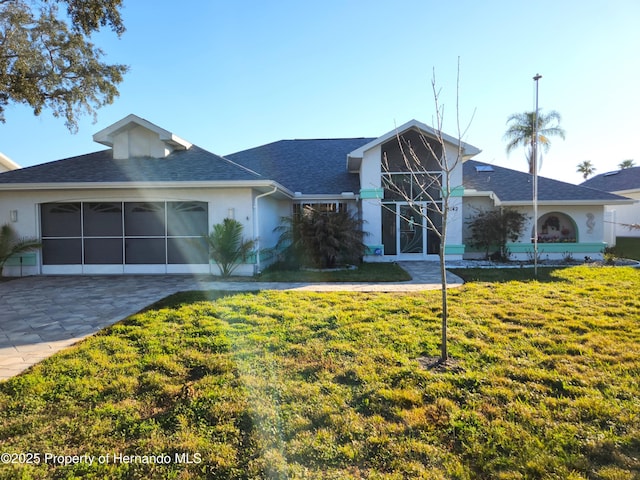 view of front of property featuring a front yard, decorative driveway, an attached garage, and stucco siding