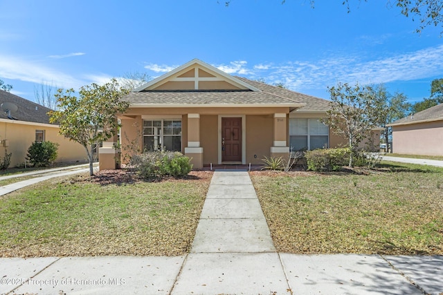 bungalow-style house with a shingled roof, a front yard, and stucco siding