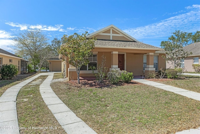 bungalow-style house with a shingled roof, a front lawn, and stucco siding