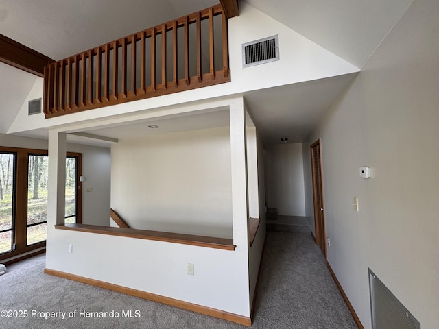 hallway with high vaulted ceiling, carpet flooring, visible vents, and baseboards