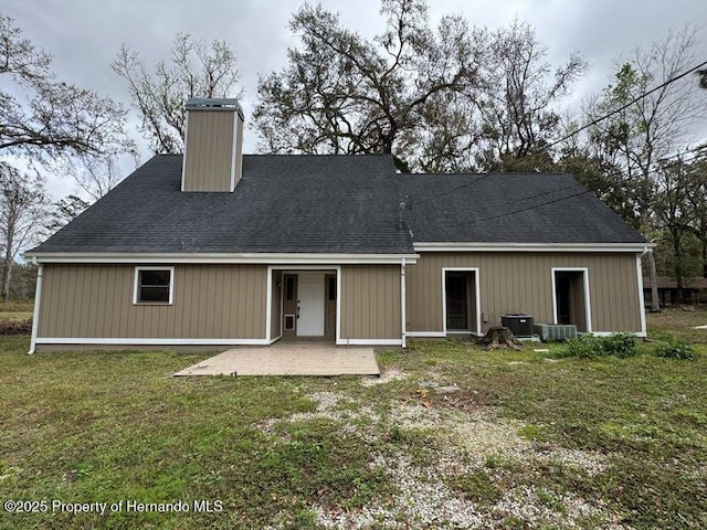 back of house with a shingled roof, a yard, a chimney, and a patio