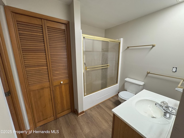 bathroom with toilet, bath / shower combo with glass door, wood finished floors, vanity, and a closet