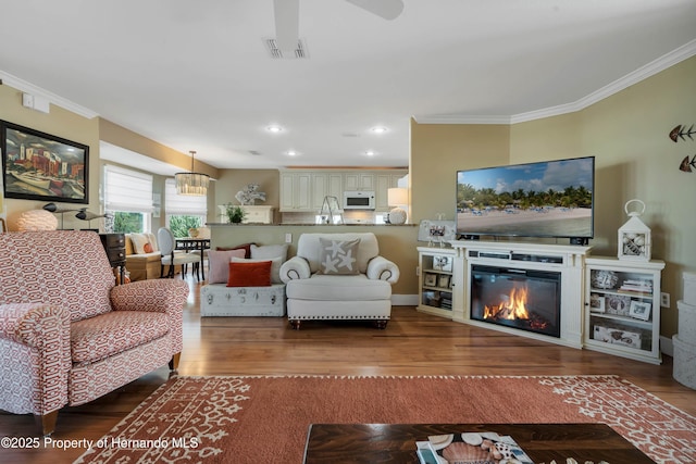 living area with recessed lighting, visible vents, ornamental molding, a glass covered fireplace, and wood finished floors