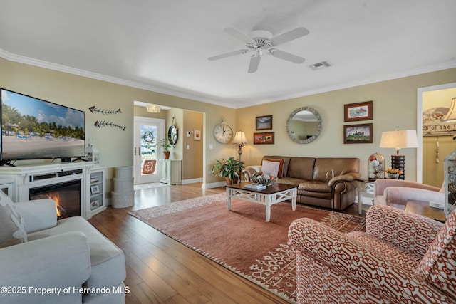 living room with visible vents, ornamental molding, dark wood-style flooring, and a glass covered fireplace