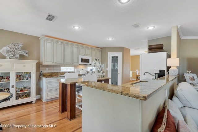 kitchen featuring visible vents, a sink, white appliances, a peninsula, and a kitchen breakfast bar