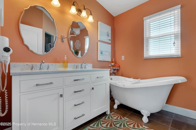 bathroom featuring double vanity, a freestanding bath, a sink, baseboards, and tile patterned floors