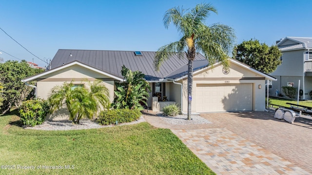 ranch-style home with metal roof, an attached garage, decorative driveway, stucco siding, and a front yard