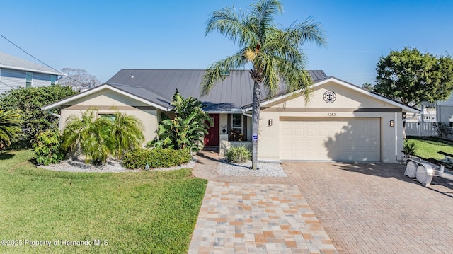 ranch-style home with decorative driveway, stucco siding, an attached garage, metal roof, and a front lawn