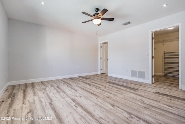 unfurnished bedroom with light wood-type flooring, visible vents, a spacious closet, and baseboards