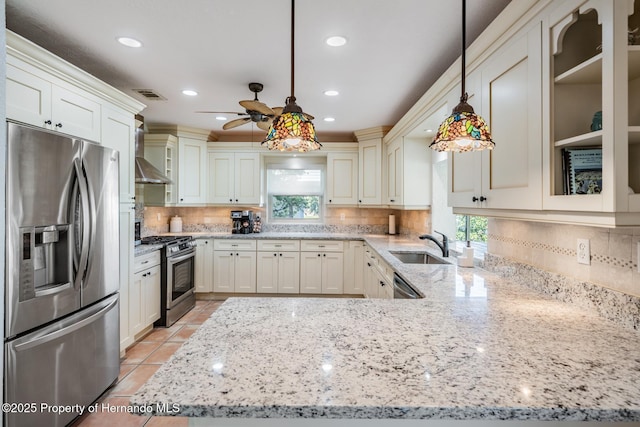 kitchen with wall chimney exhaust hood, appliances with stainless steel finishes, plenty of natural light, and decorative light fixtures